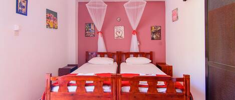 A double bed with a wooden frame and white bedding, two mosquito nets, and a red rug on the floor.