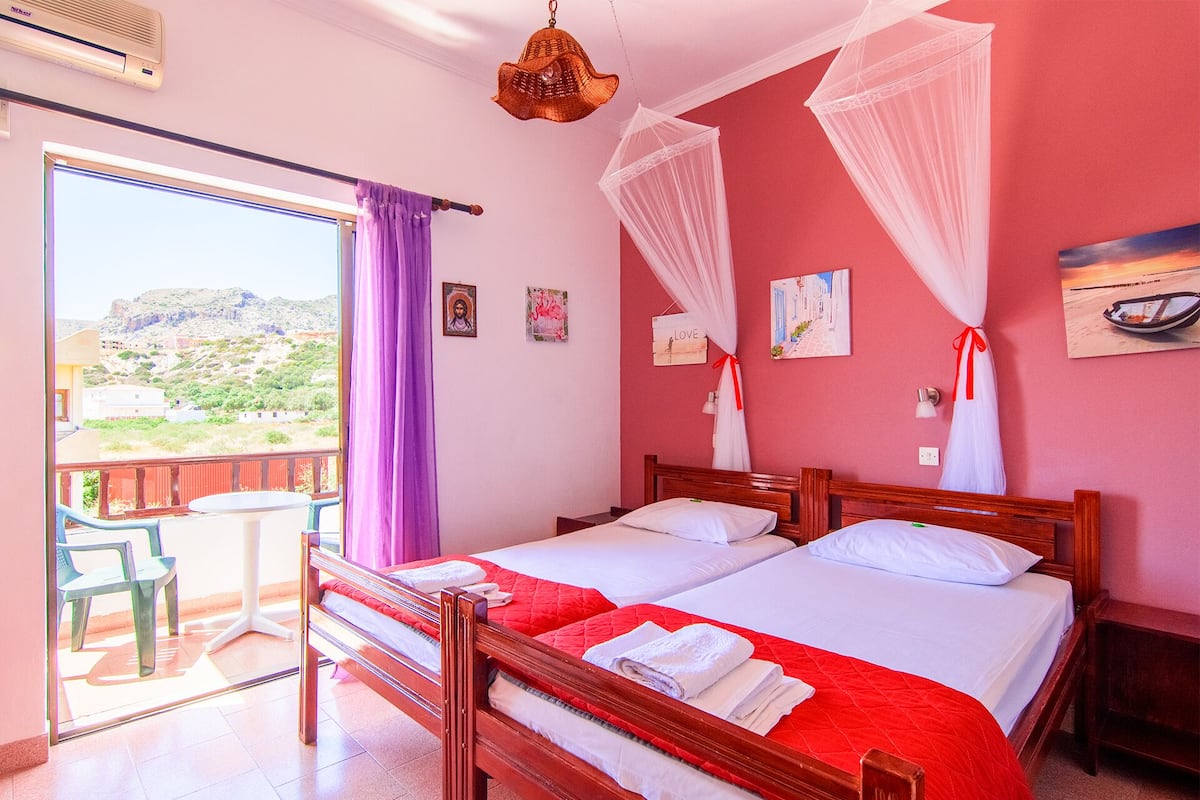 Een slaapkamer met twee bedden, een balkon met uitzicht op het landschap en een klamboe over de bedden.