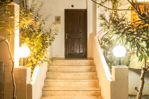 A staircase leading to a dark wooden door, flanked by plants and illuminated by two spherical lights.