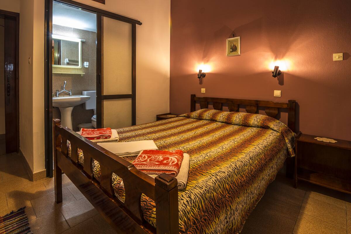 Een slaapkamer met een bed, een nachtkastje, een wandlamp en een badkamer die door een open deur zichtbaar is.