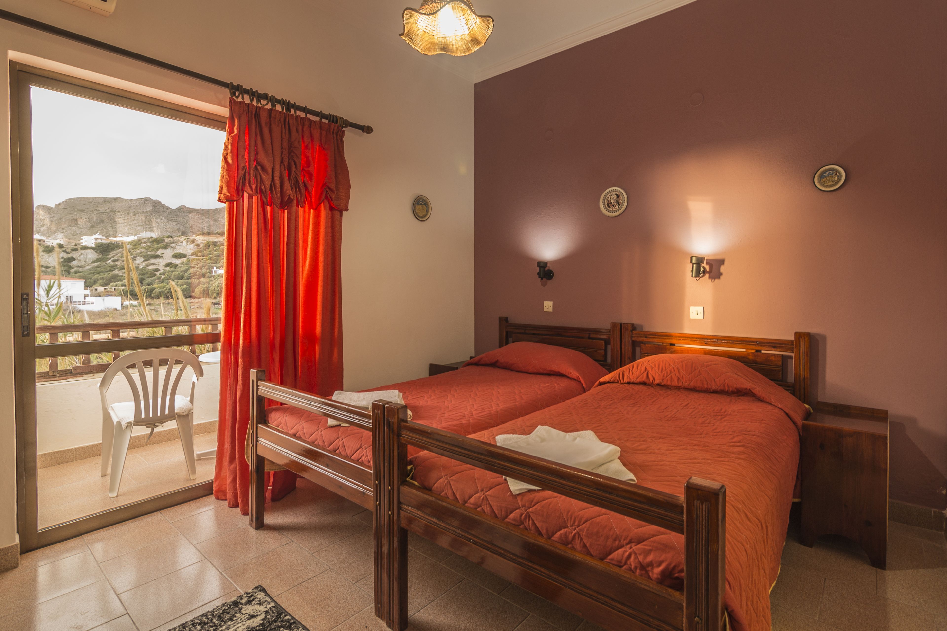 A room with a bed, a chair, a window with curtains, and a view of the outside.