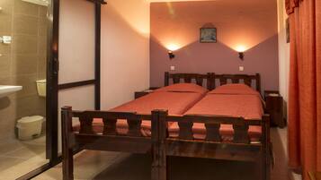 A bedroom with a wooden bed, two bedside tables, a nightstand, a wall-mounted light, and a bathroom visible through an open door.