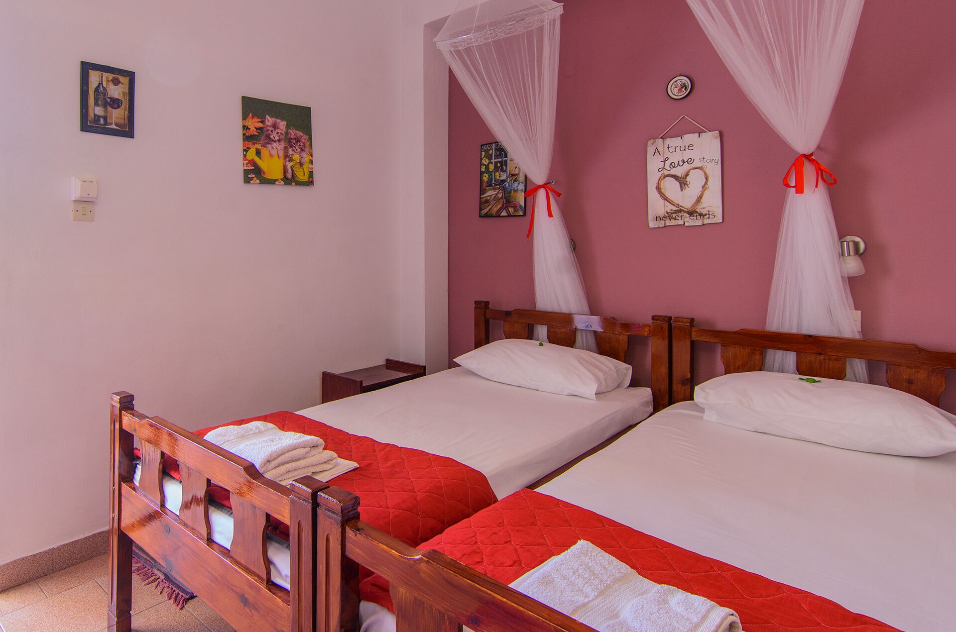 Un dormitorio con dos camas individuales, cabecera de madera, colcha acolchada roja, almohadas blancas y mosquitero.
