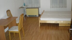 Una habitación con una cama de madera, un escritorio de madera, una silla, una mesita con una lámpara y un radiador.