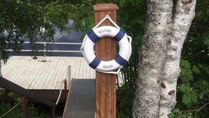A wooden dock with a lifebuoy hanging from a post, surrounded by trees and a body of water.