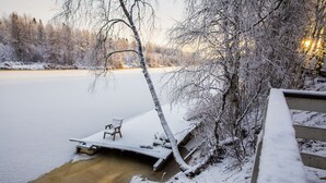 A snowy lakeside scene with a dock and a bench.