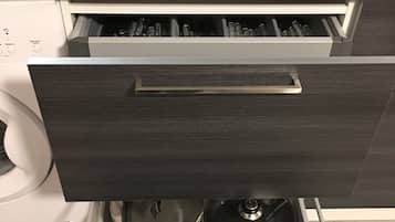 A kitchen with a built-in stove, a sink, and a drawer with kitchen utensils.