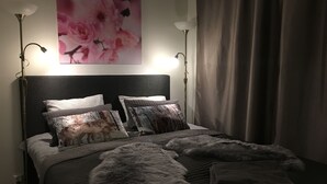 A bedroom with a bed, pillows, a blanket, a painting, and two floor lamps.