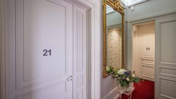 A hallway with white doors numbered 21 and 22, a large ornate mirror, and a clear stand with flowers.