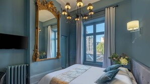 Habitación de hotel con una cama grande, un candelabro, un espejo amplio y vistas al exterior.