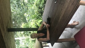 Eine Person sitzt draußen an einem Holztisch mit Blick auf dichtes Grün.