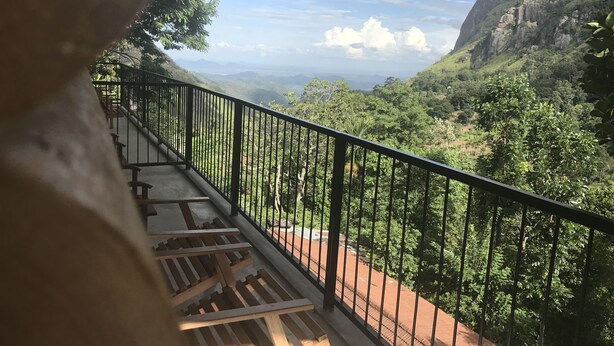 Ein Balkon mit Metallgeländer, der auf ein üppiges Tal mit entfernten Bergen und einem klaren Himmel blickt.