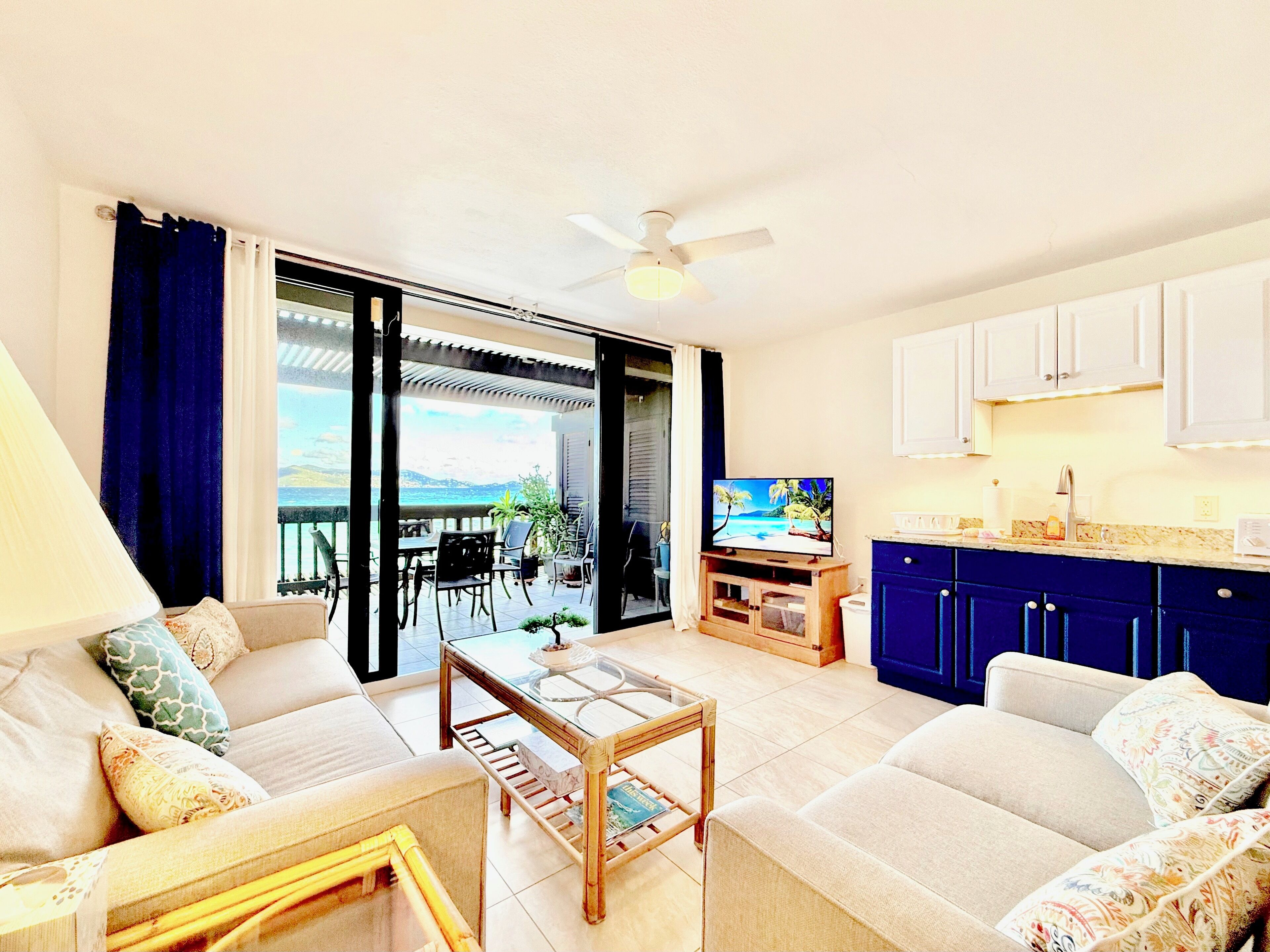 Ein Wohnzimmer mit Sofa, Couchtisch und Fernseher. Ein Balkon bietet Blick auf das Meer.