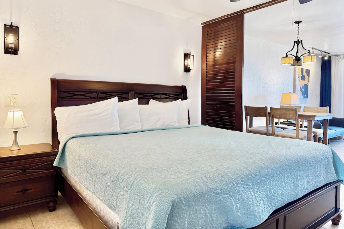A neatly made bed with a patterned bedspread, a wooden headboard, and a nightstand with a lamp.