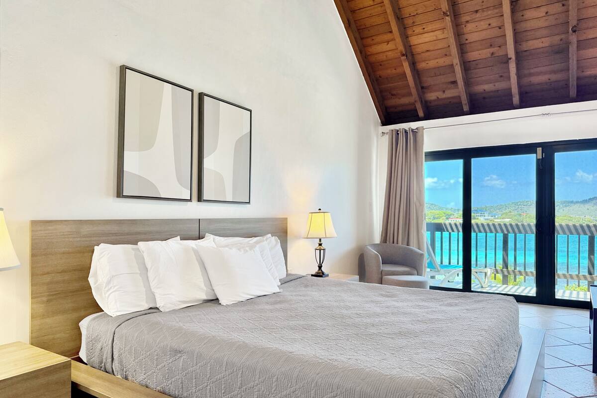 A hotel room with a large bed, a chair, and a view of the sea.