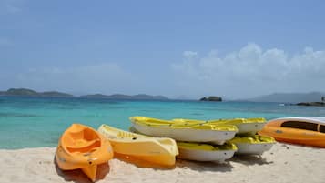 Une plage où plusieurs kayaks sont alignés sur le sable, un ciel bleu clair et des montagnes qui se dessinent à l’horizon.