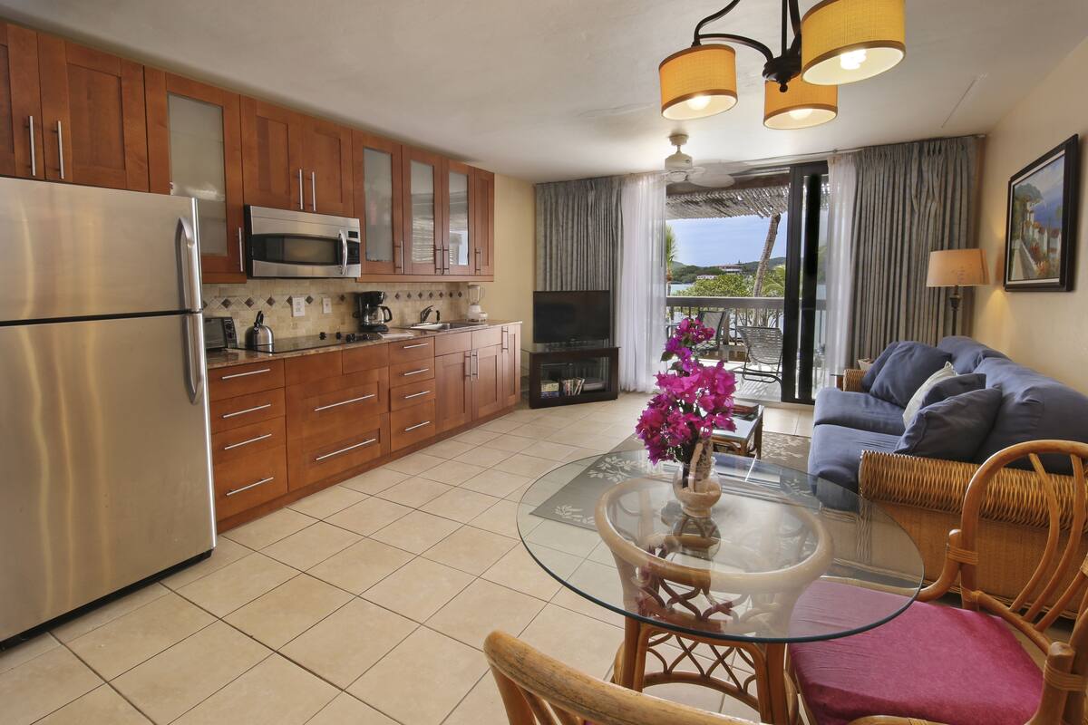 A modern kitchen with wooden cabinets, stainless steel appliances, and a glass dining table with chairs.