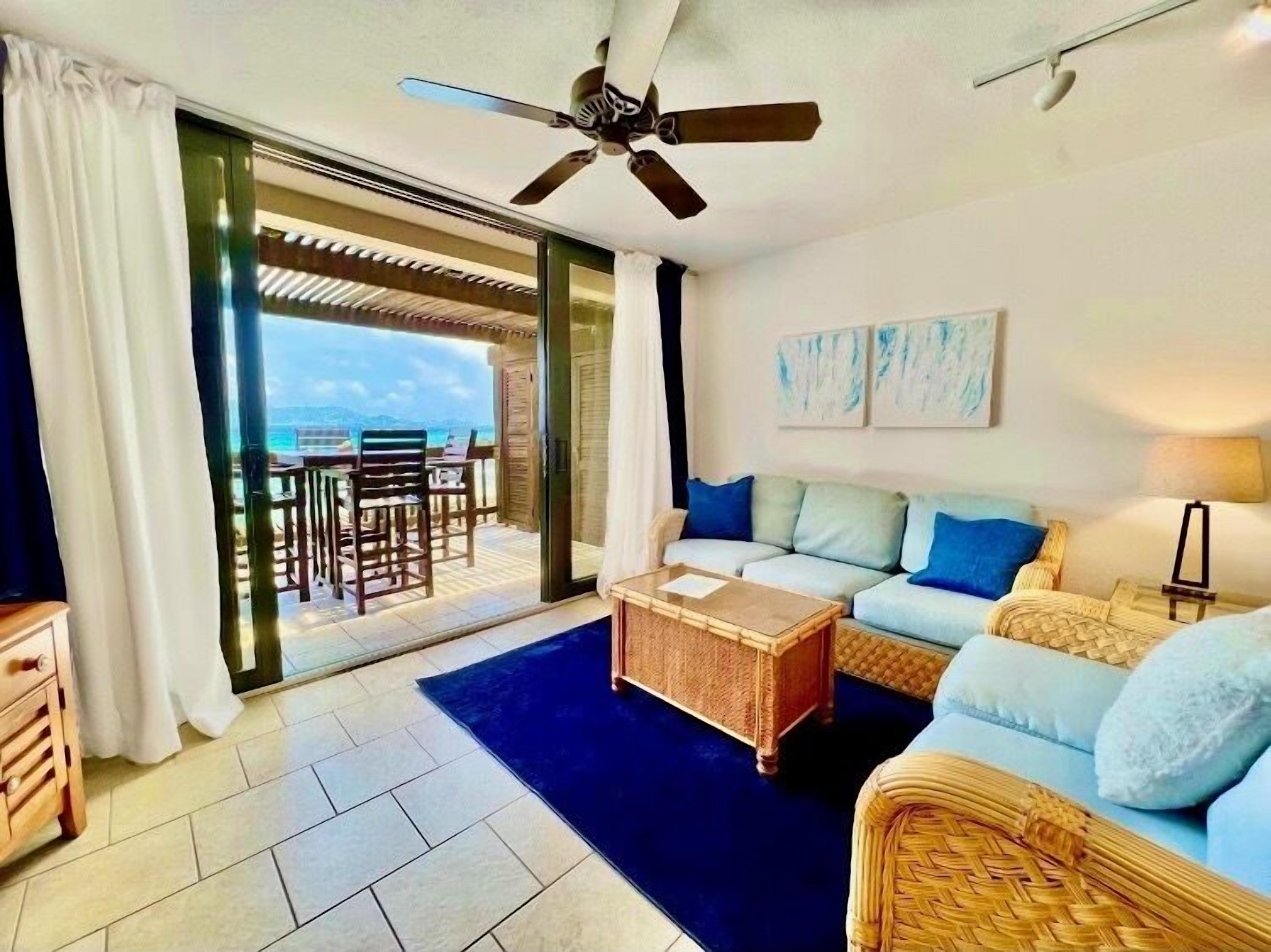 A room with a sofa, coffee table, and a view of the ocean through a sliding glass door.