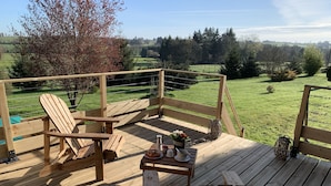 Een houten terras met een tafel en stoelen, met uitzicht op een groen landschap.