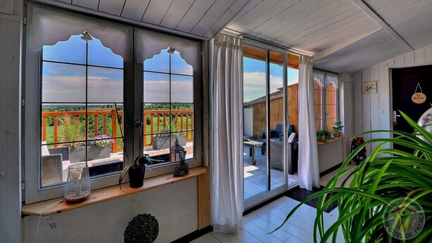 Een kamer met grote ramen, een balkon met tuinmeubilair en uitzicht op groen.