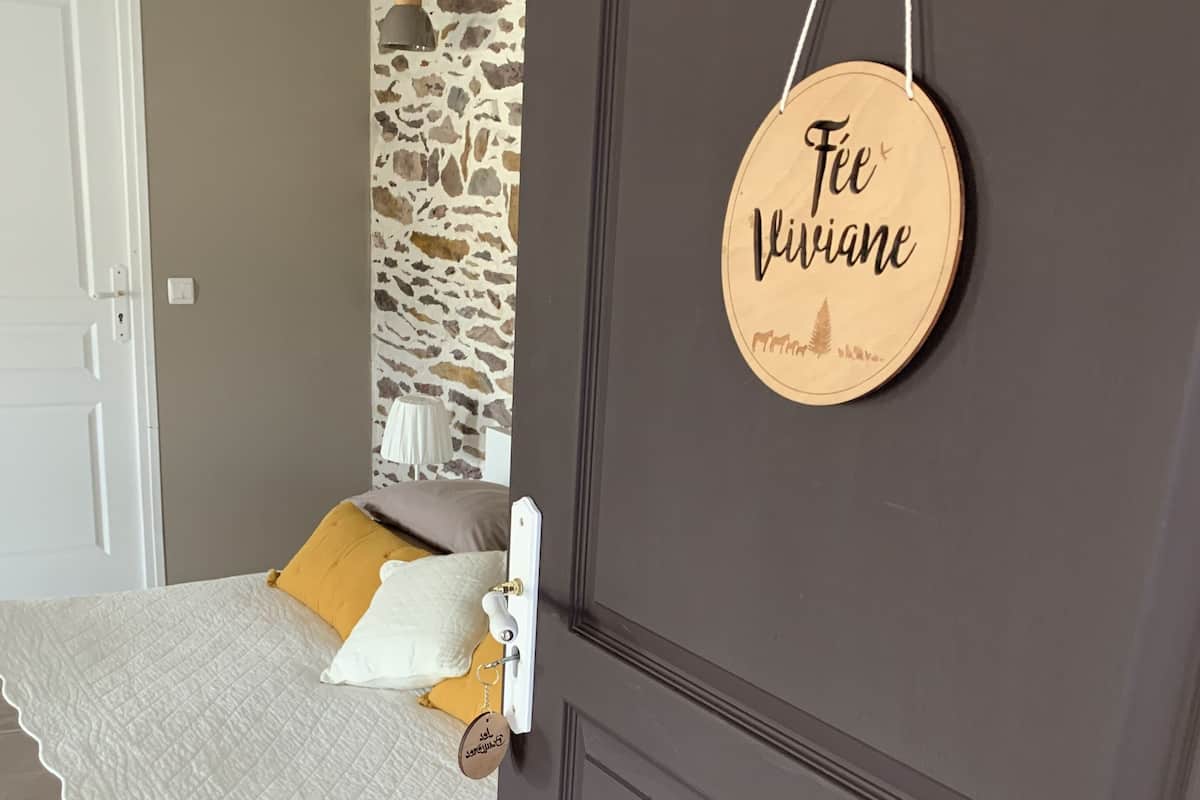 A bedroom with a bed, a wooden door with a sign, a stone wall, and a white door.