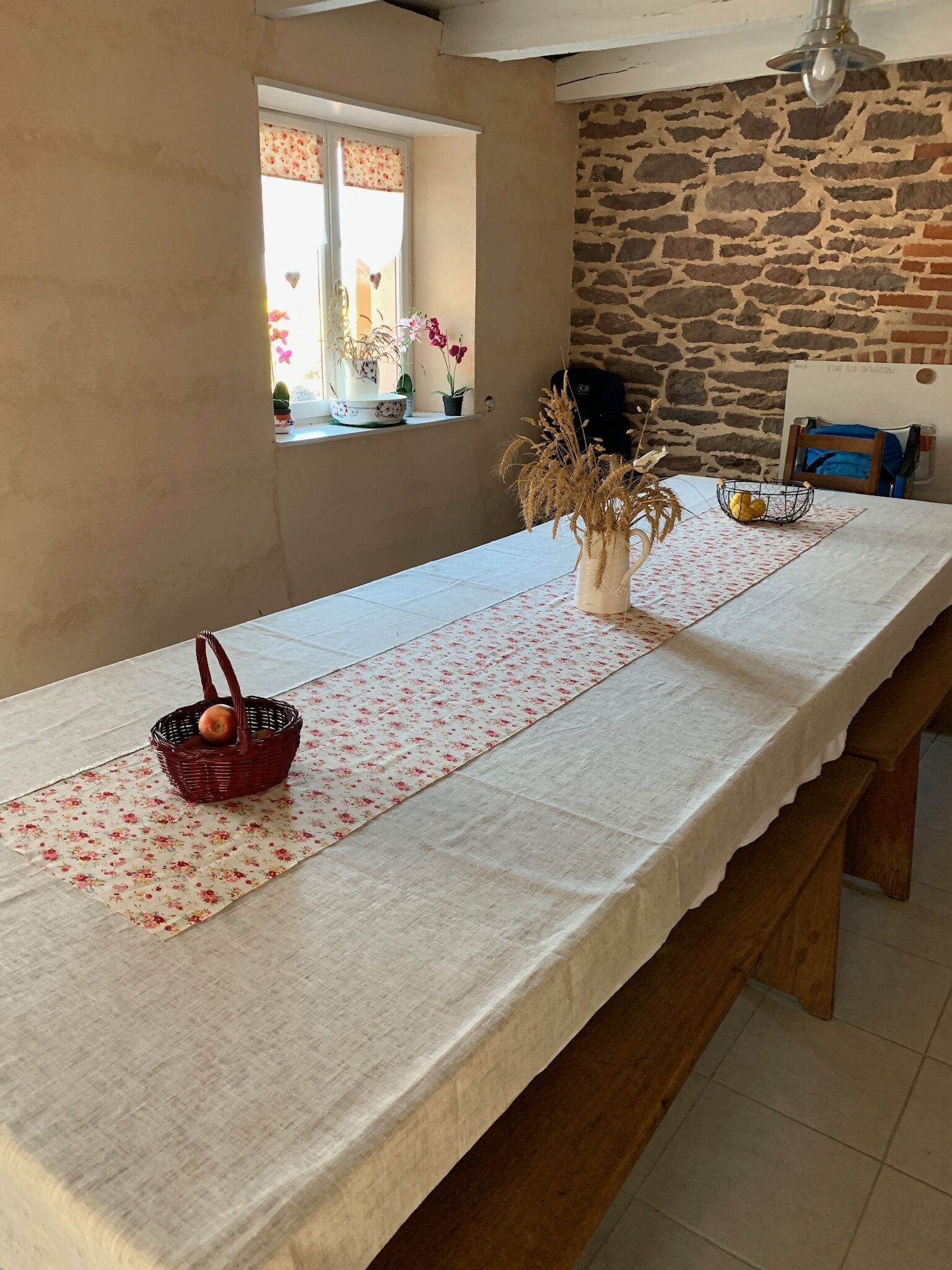 A long dining table with a white tablecloth, a floral runner, and a basket with an apple.