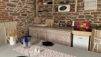 A kitchen with a stone wall, wooden shelves, a microwave, and a small refrigerator.