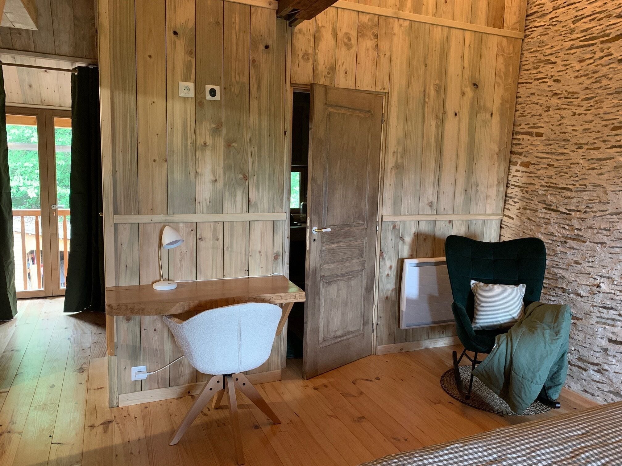 A rustic wooden room with a desk, chair, and a bed.