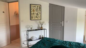 Quarto com colcha verde, uma impressão botânica emoldurada na parede, mesa de cabeceira com abajur e uma porta.