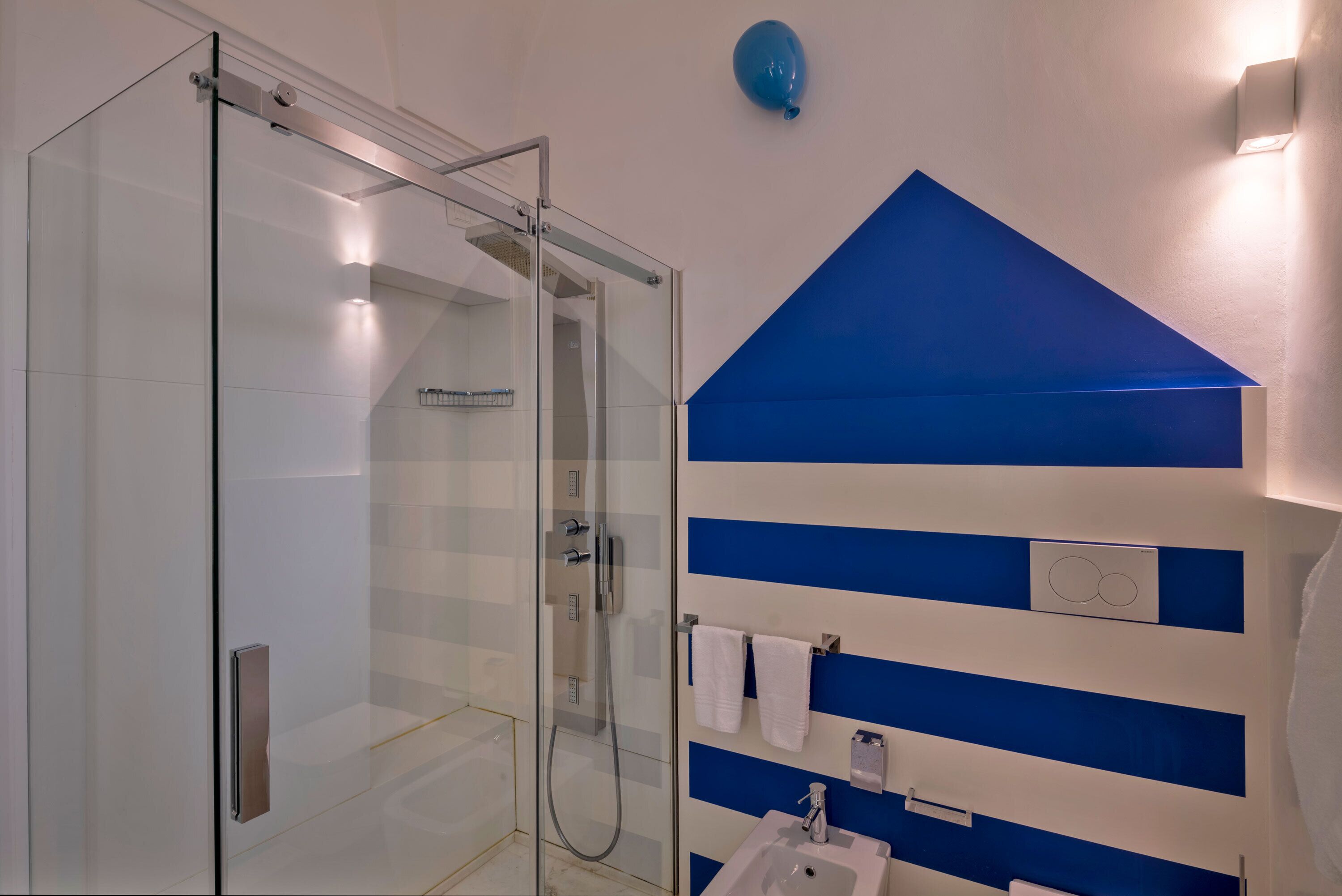 A modern bathroom with a glass shower enclosure, a sink with a mirror, and a blue and white striped wall design.
