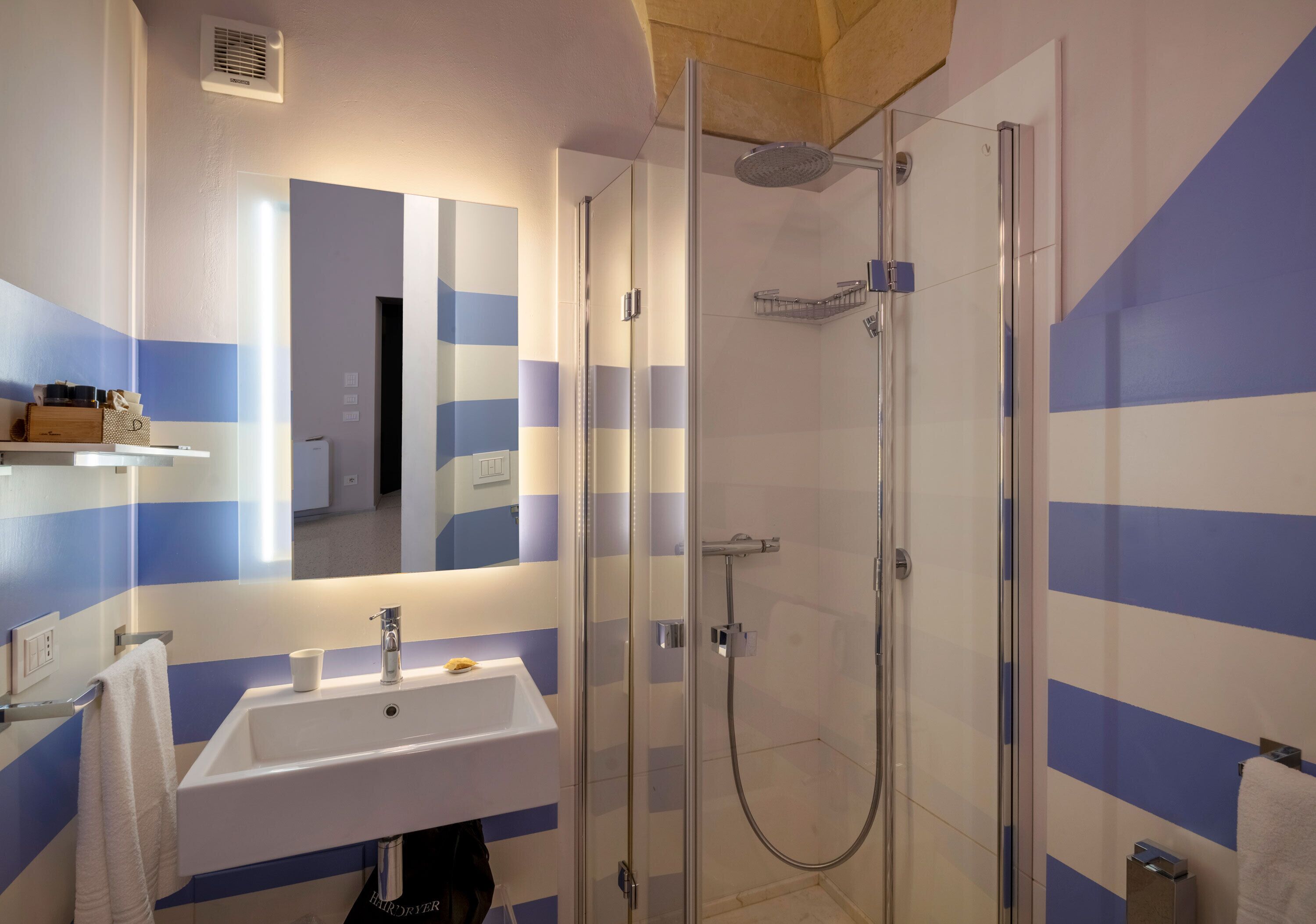 A modern bathroom with a glass-enclosed shower, a white sink, and striped walls.