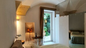 A bedroom with a bed, a desk, a lamp, and a view of greenery outside.