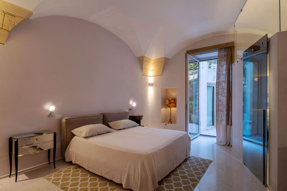 Un dormitori modern amb llit, taules de nit i una porta de vidre que dona a un balcó.