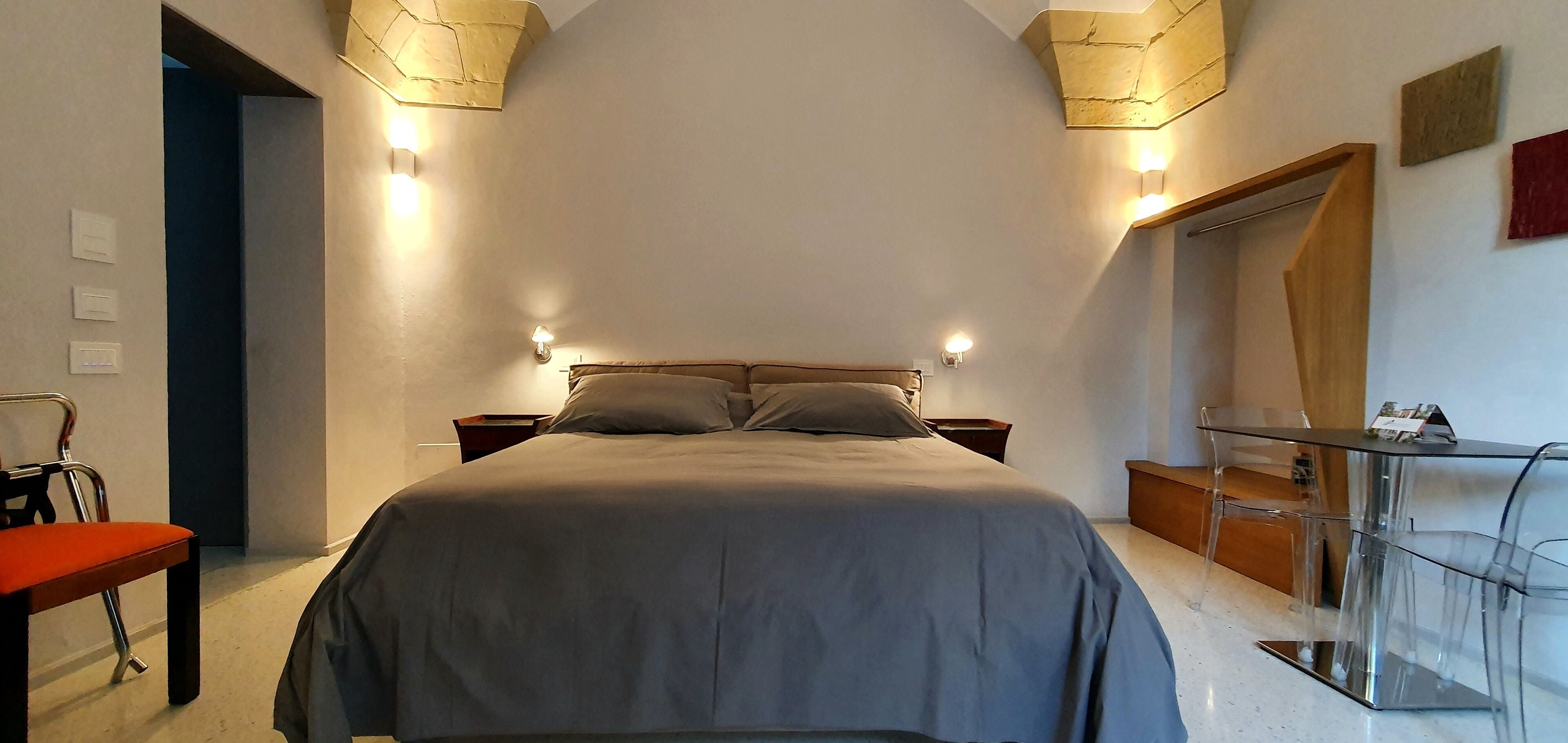 A bedroom with a bed, bedside tables, a desk with a chair, and a mirror.