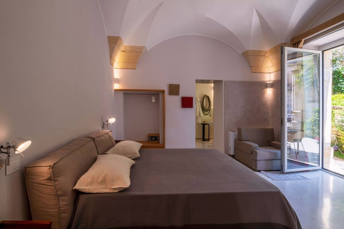 Un dormitori modern amb un llit gran, un sofà i una porta de vidre que dona a un balcó.