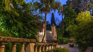 A garden with a stone balustrade, potted plants, and a pathway leading to a building.