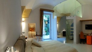 A modern bedroom with a large bed, a desk, and a glass-enclosed bathroom.
