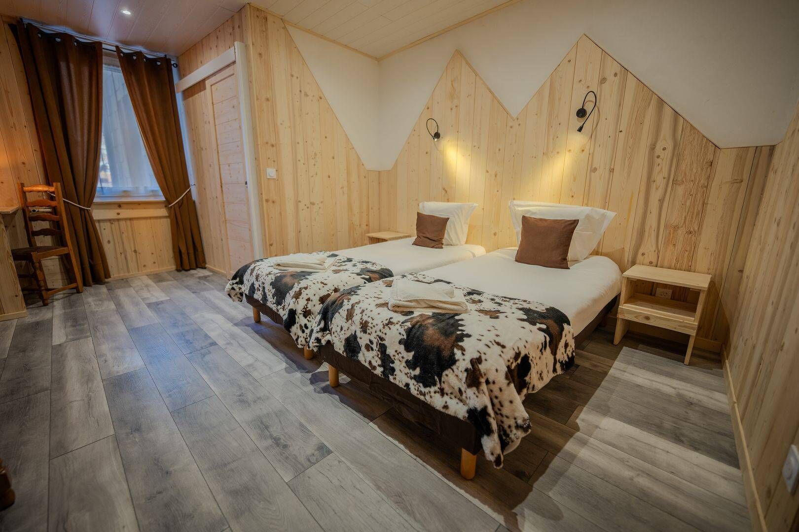 A wooden-paneled bedroom with two beds, a wooden ladder, and a small wooden nightstand.