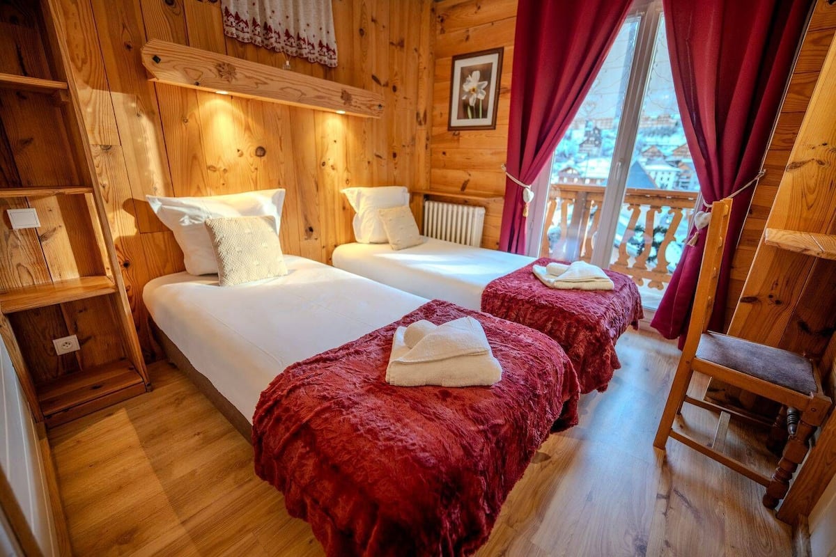 Una cabaña de madera con dos camas, una colcha roja, una escalera de madera y una ventana con vistas.