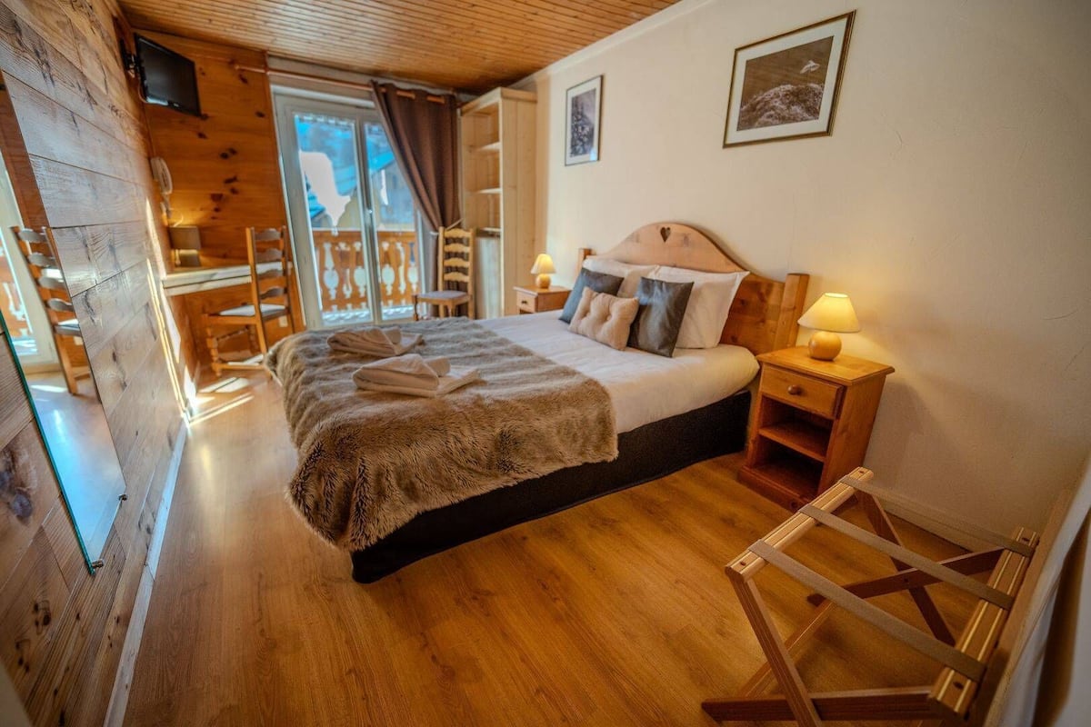 Una habitación acogedora de madera con una cama, una mesita de noche y un ventanal con cortinas.