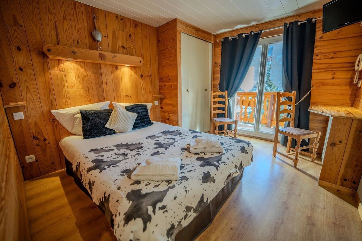 Habitación de cabaña de madera con cama, una silla, un escritorio y un balcón con vistas.