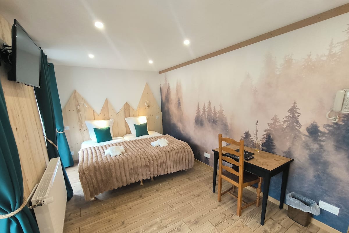 Una habitación con cama, escritorio, silla, televisión y un mural en la pared.