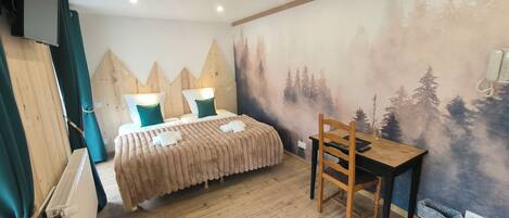 Una habitación con cama, escritorio, silla, televisión y un mural en la pared.
