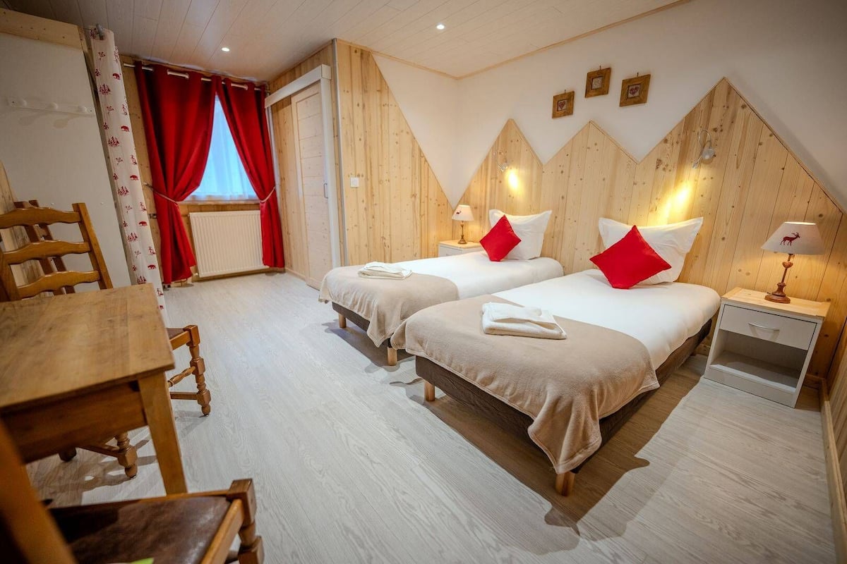 Habitación de hotel con dos camas, una mesa de madera y una silla.