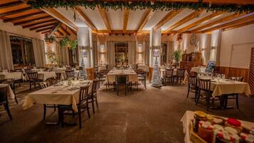 Un restaurant avec des poutres en bois, des tables dressées pour le dîner et un sapin de Noël.
