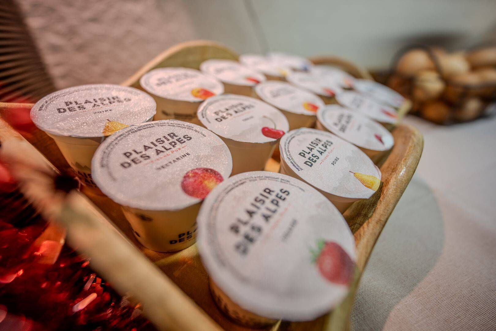 A wooden tray with several containers labeled 'PLAISIR DES ALPES' containing what appears to be a food product.