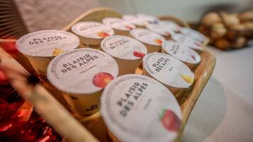 A wooden tray with several containers labeled 'PLAISIR DES ALPES' containing what appears to be a food product.