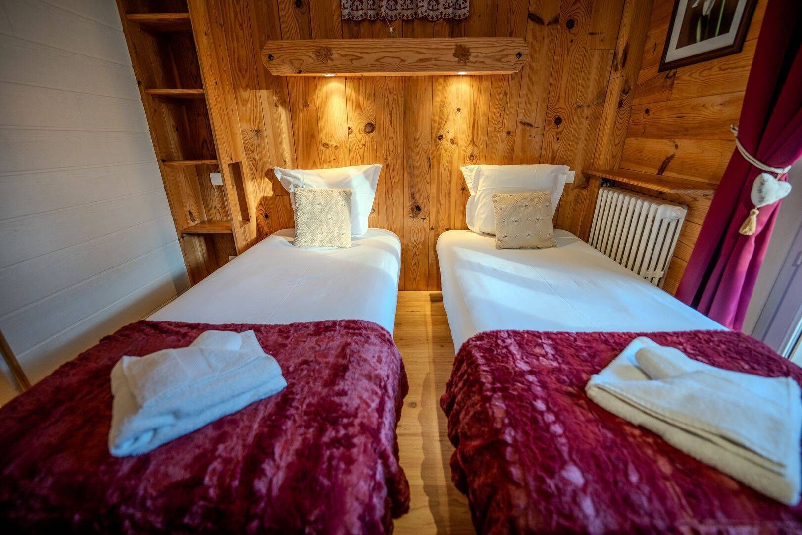 Une chambre avec deux lits, chacun recouvert d’une couverture rouge et doté d’oreillers blancs, des murs en bois et une étagère en bois au-dessus des lits.