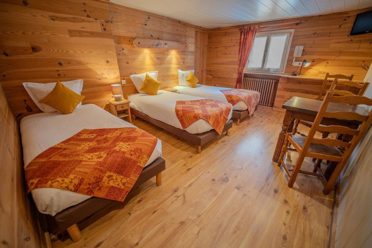 Una habitación de cabaña de madera con tres camas, una mesa de madera y una silla.
