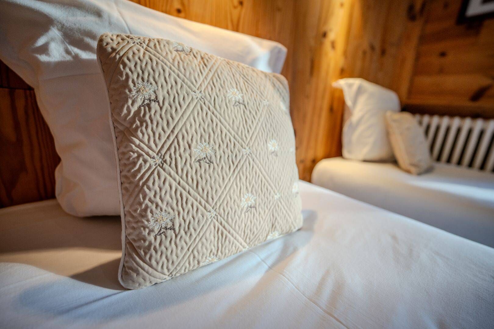 Ein Bett mit einem gesteppten Kopfkissen und einer weißen Daunendecke in einem Zimmer einer Holzhütte.